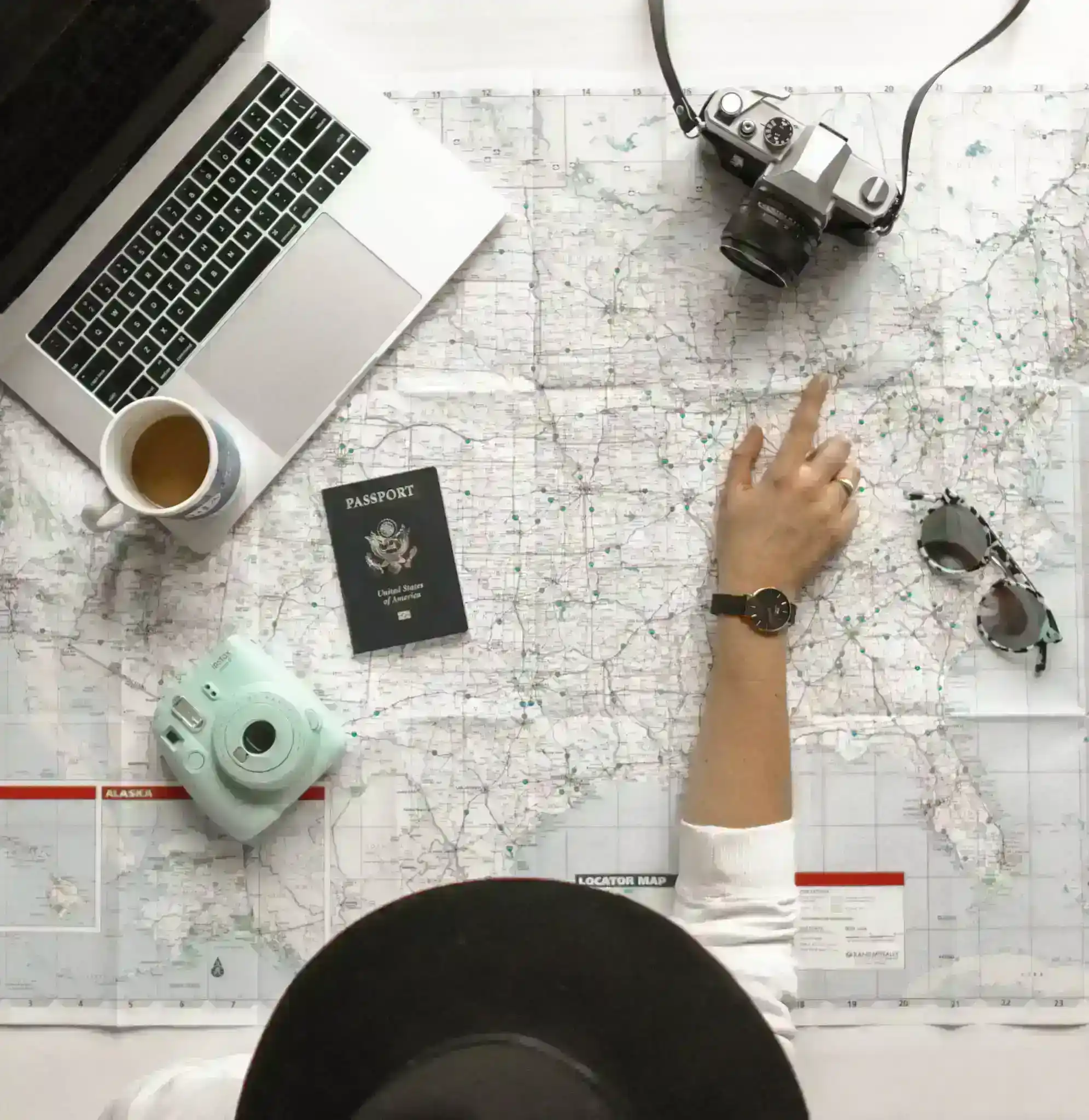 top view of person sitting at a desk with a map, laptop, cofee, camera and passport