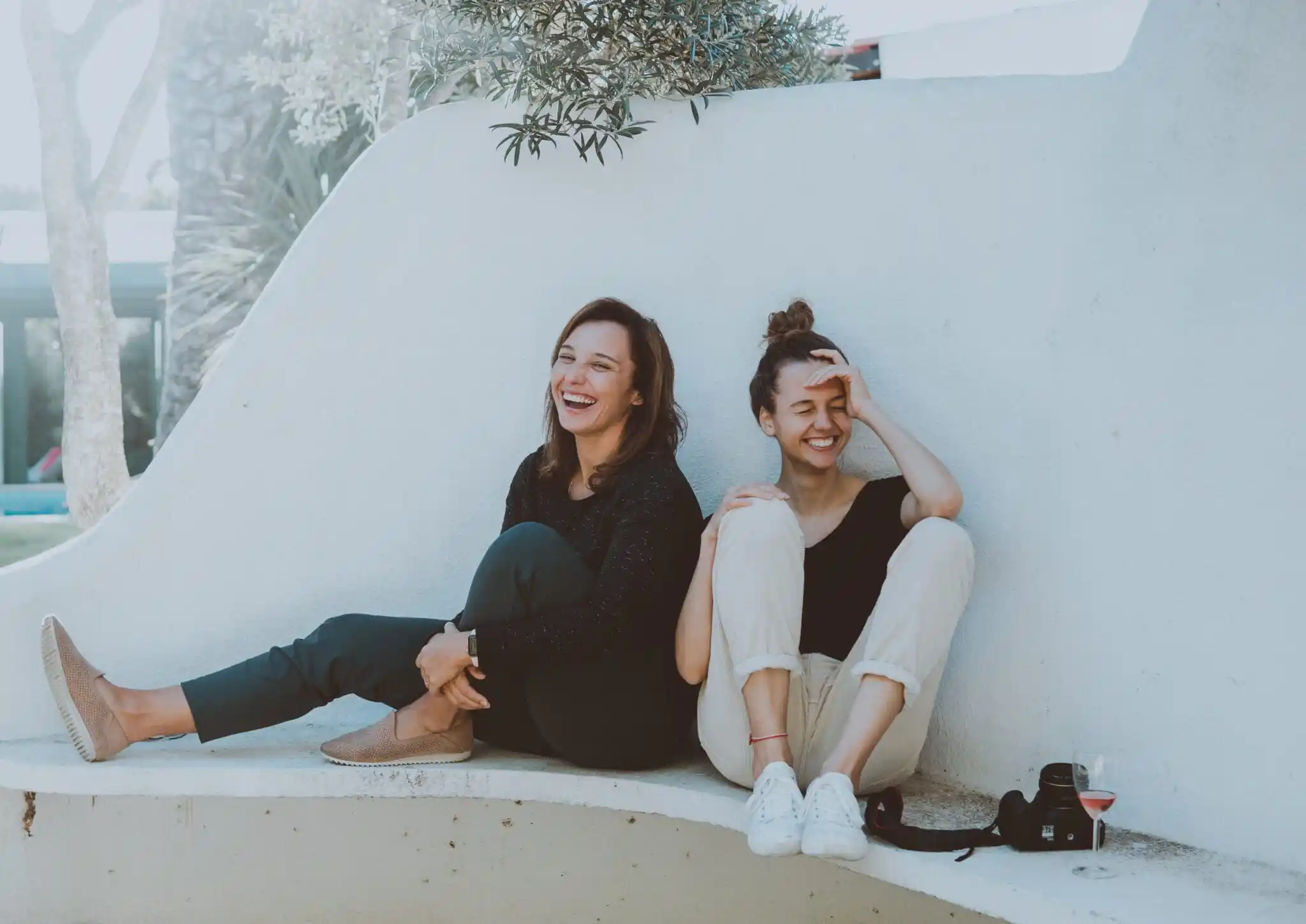 two friends sitting next to a wall chatting and laughing