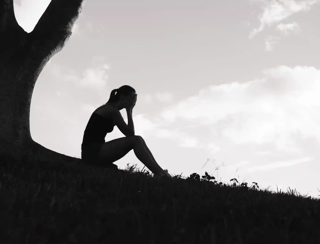 silhouette of woman sitting under a tree with head in hands - depression