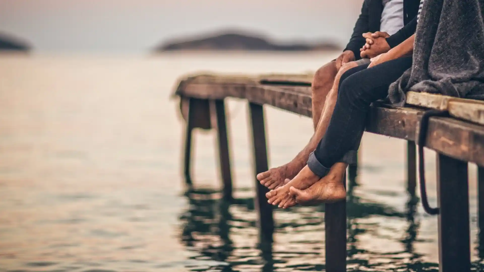people sitting with their legs hanging off a pier at a lake