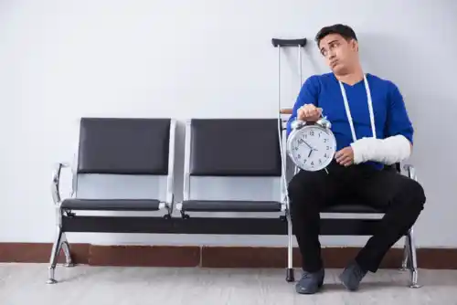 man sitting in hospital waiting room with broken arm and crutch behind him
