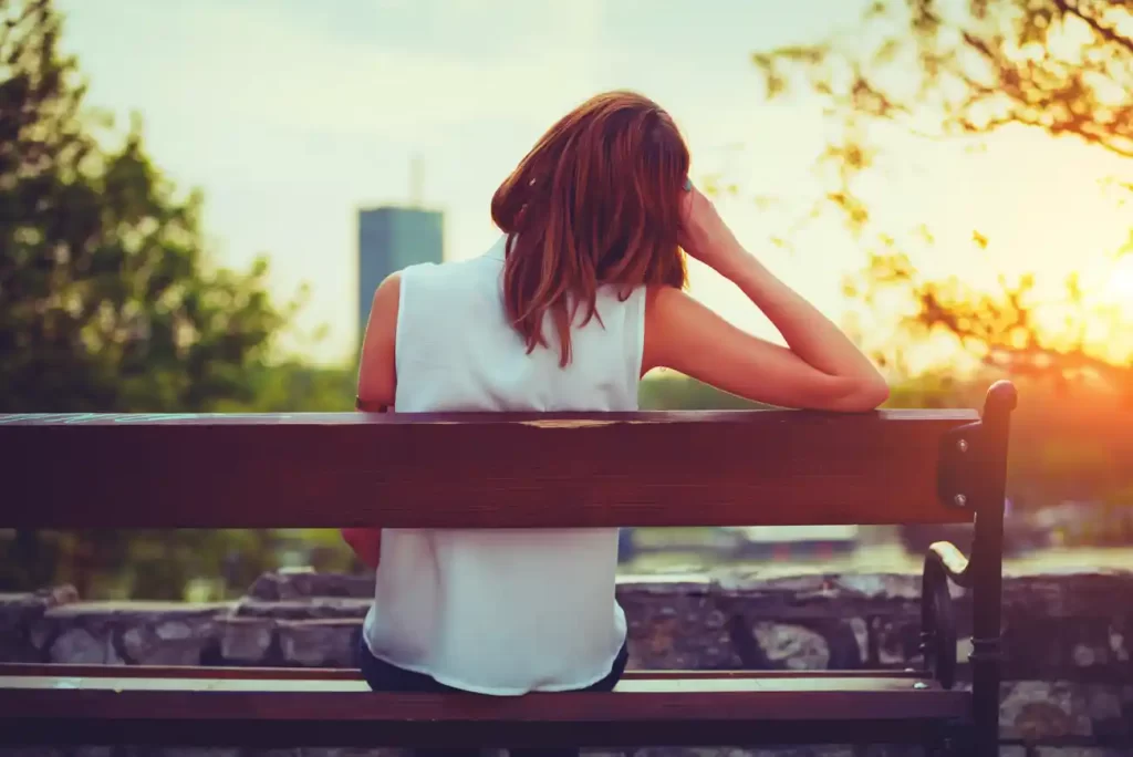 woman sitting on a park bench looking at sunset over the city leaning her head on her hand