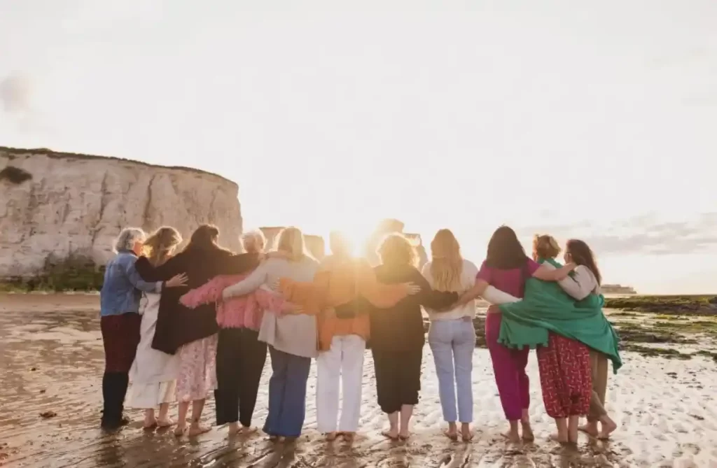 women standing together with arms around each other on the beach at sunset