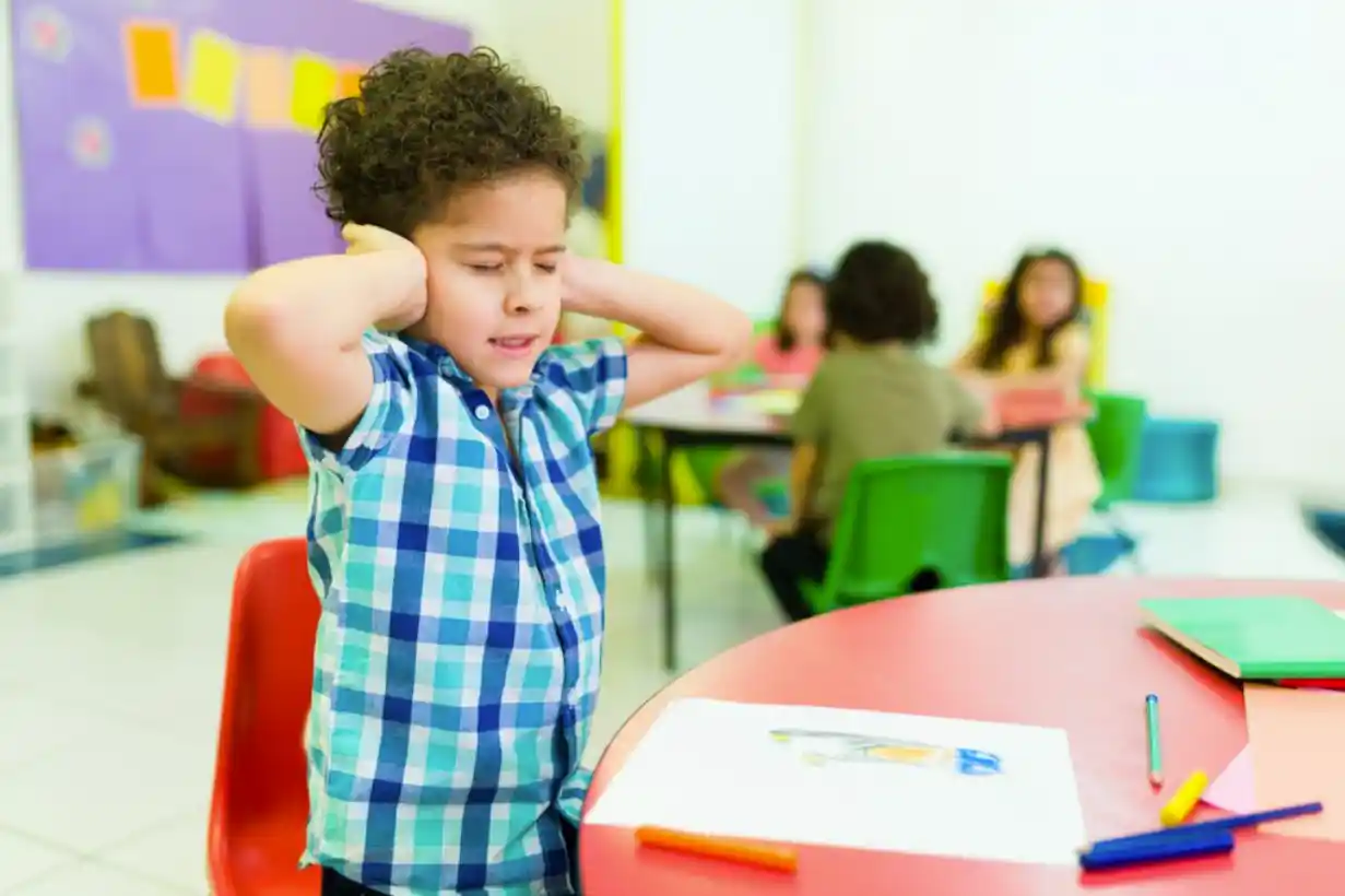 child in preschool pressing both hands against his ears