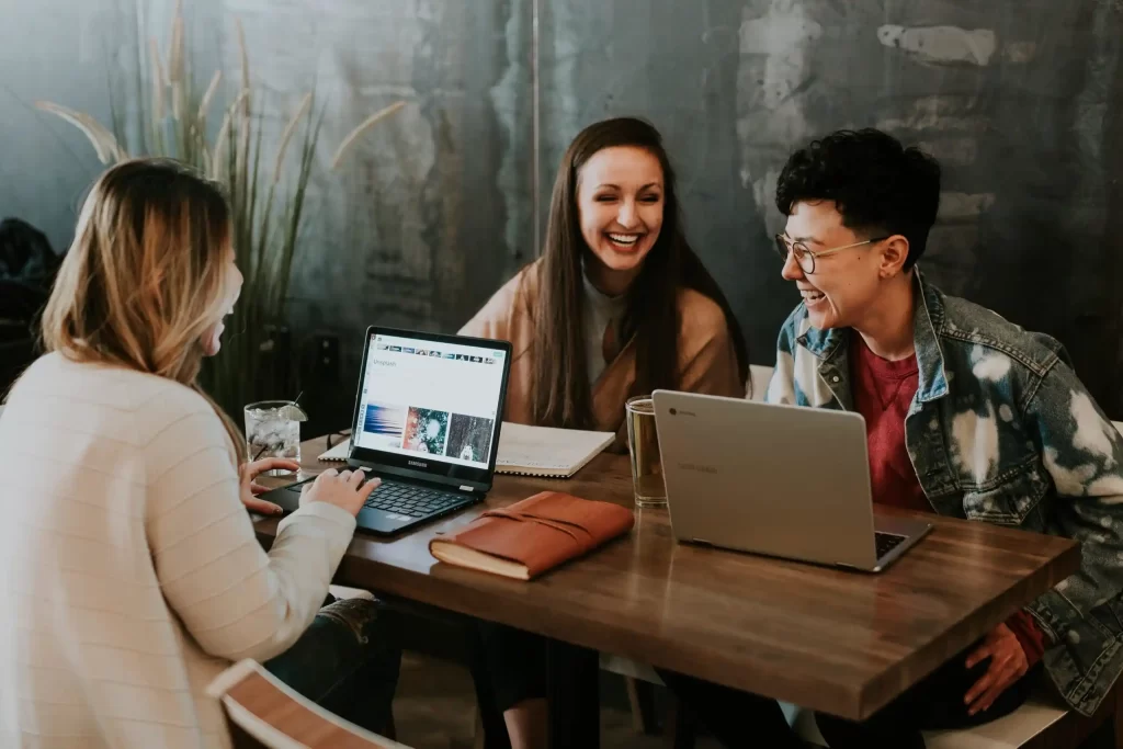 group of women sitting around a table with laptops and laughing