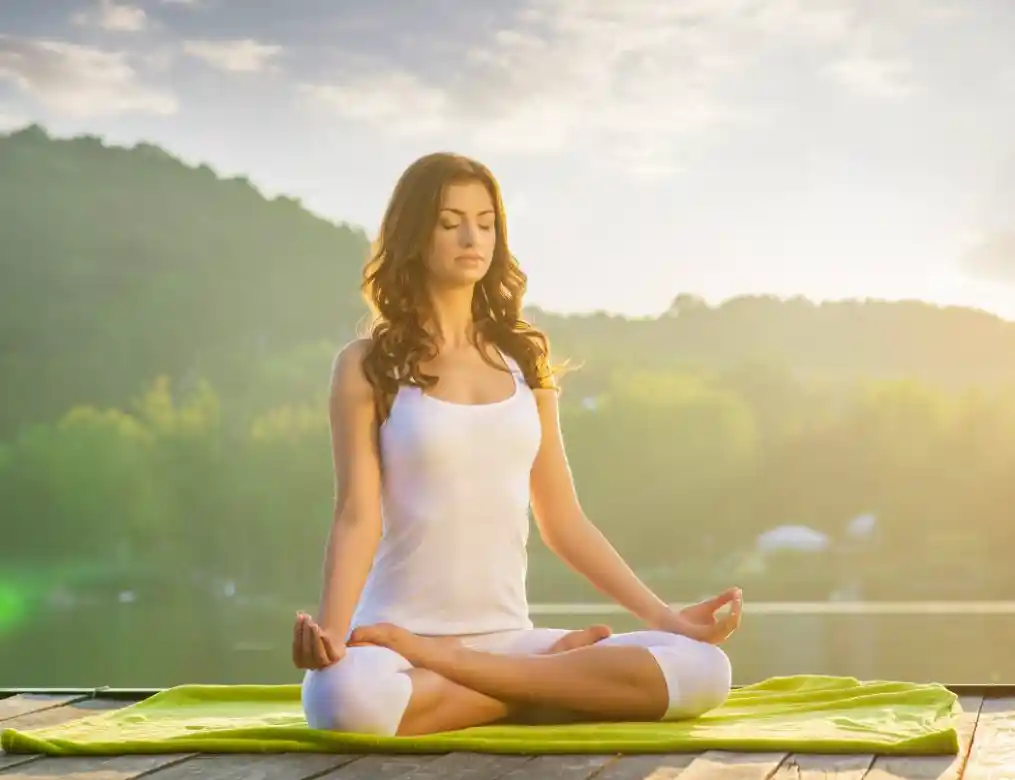 woman meditating with mountains and sun in the background