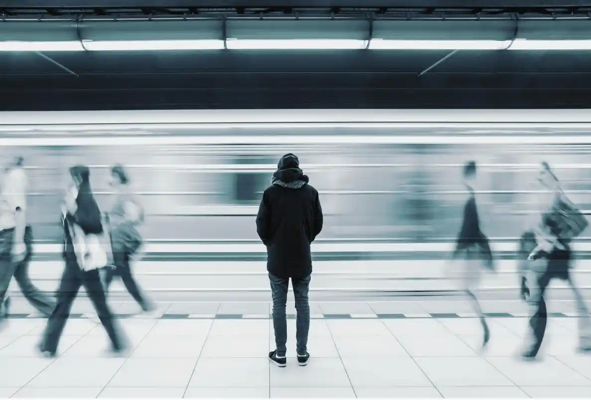 man standing on metro station platform with people walking around and a fast moving train passing by